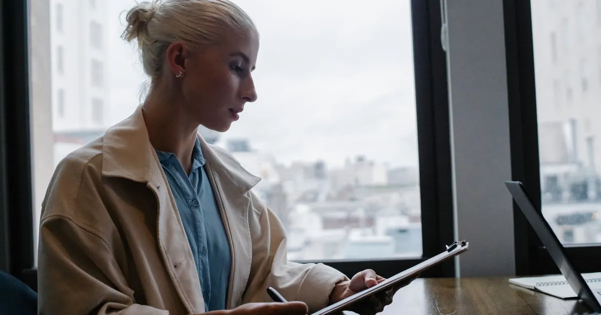 Professional reviewing files on a tablet beside a laptop in an office