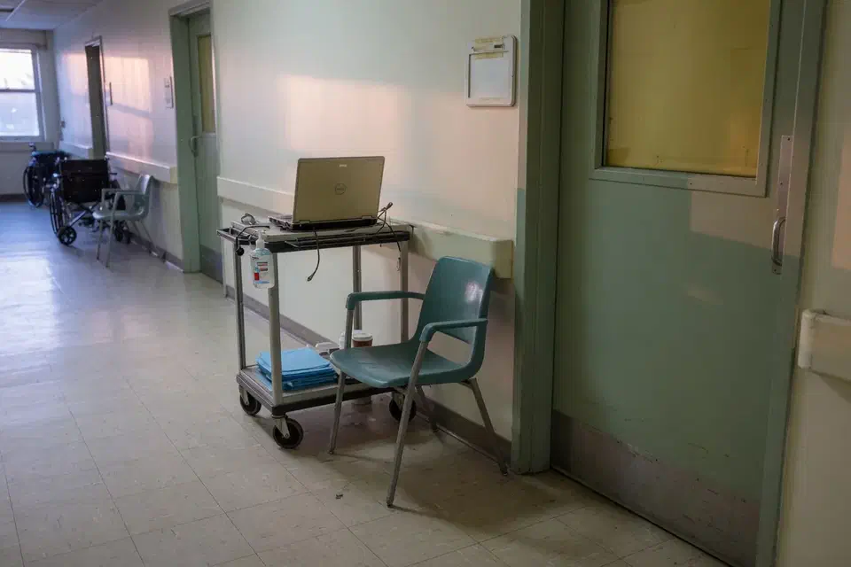 Quiet clinic hallway with a laptop cart outside an exam room at dawn