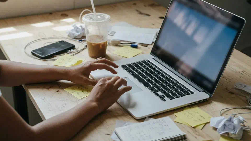 Hands on a laptop at a messy small-business desk, screen out of focus